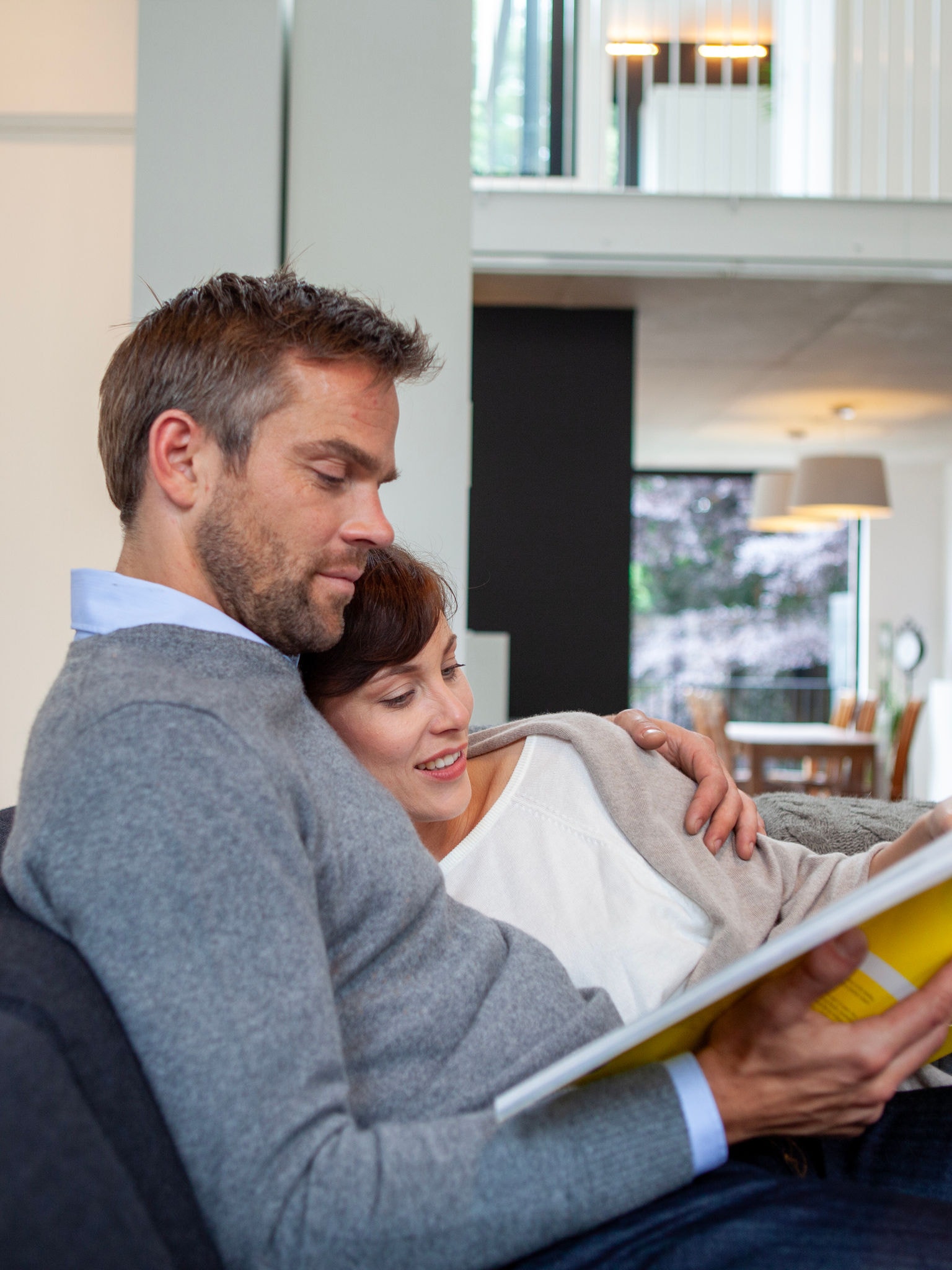 Couple cuddling and relaxing on their couch while reading a book in perfect temperature