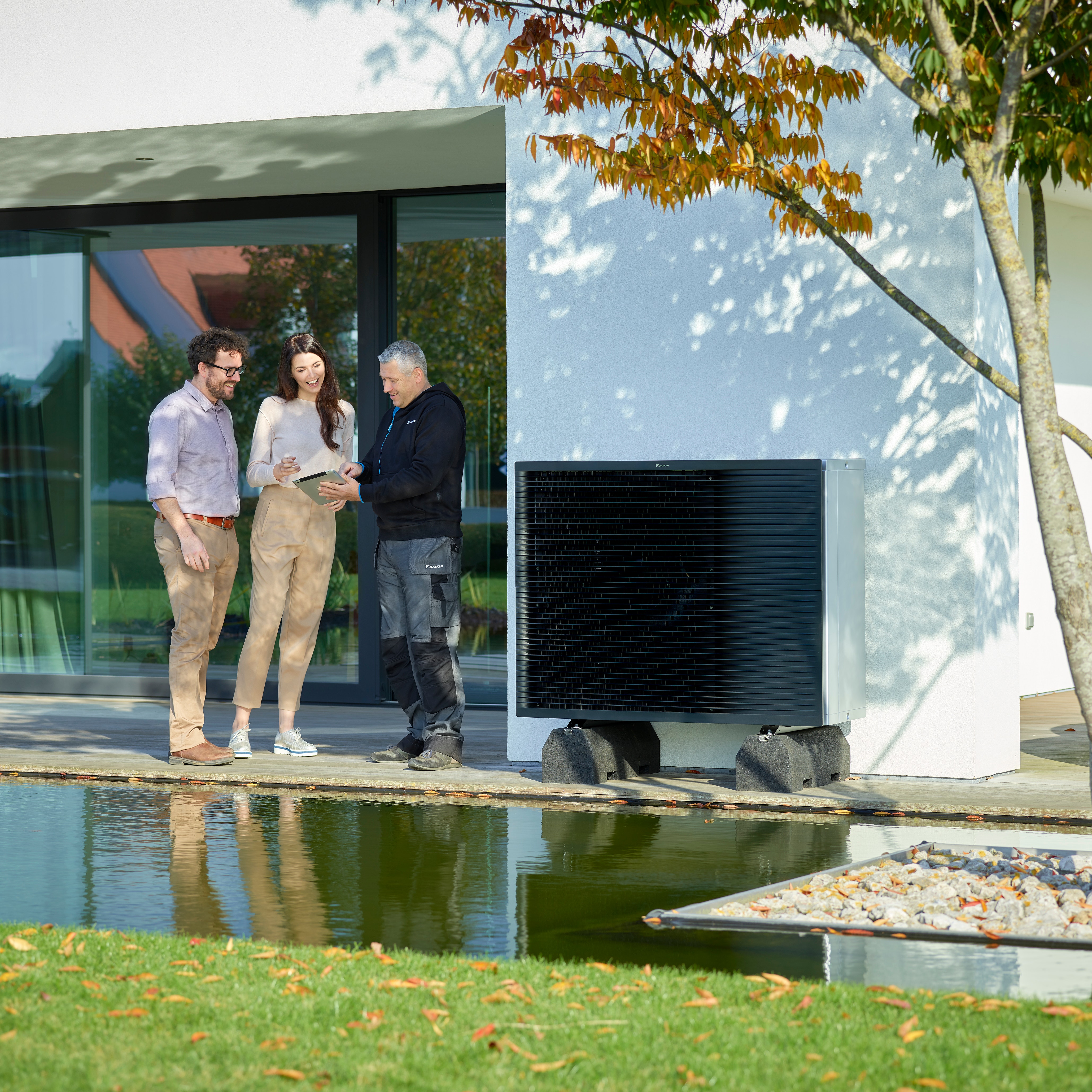 A couple with installer discussing the installation of a heat pump system outside their modern home